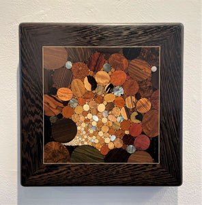 This fabulous piece of wood wall art is made of more than 100 different types of wood and shells all in small round and roundish pieces all tightly inlaid together in an abstract pattern.  There are many shades of browns predominantly along with a bit of black and with glints of silver, blue and green iridescence from the shells that are included.  It has a brown wood border with a beautiful grain.  