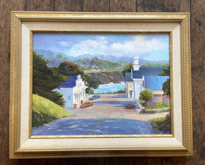 View from the hill down to the sea on a sunny day, with trees casting shadows, and clouds cooling the sky. Framed image.