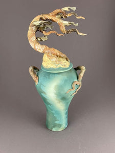 Tall ginger jar with lid. Cypress tree tops the lid with tree branch handles on a soft teal and green jar.